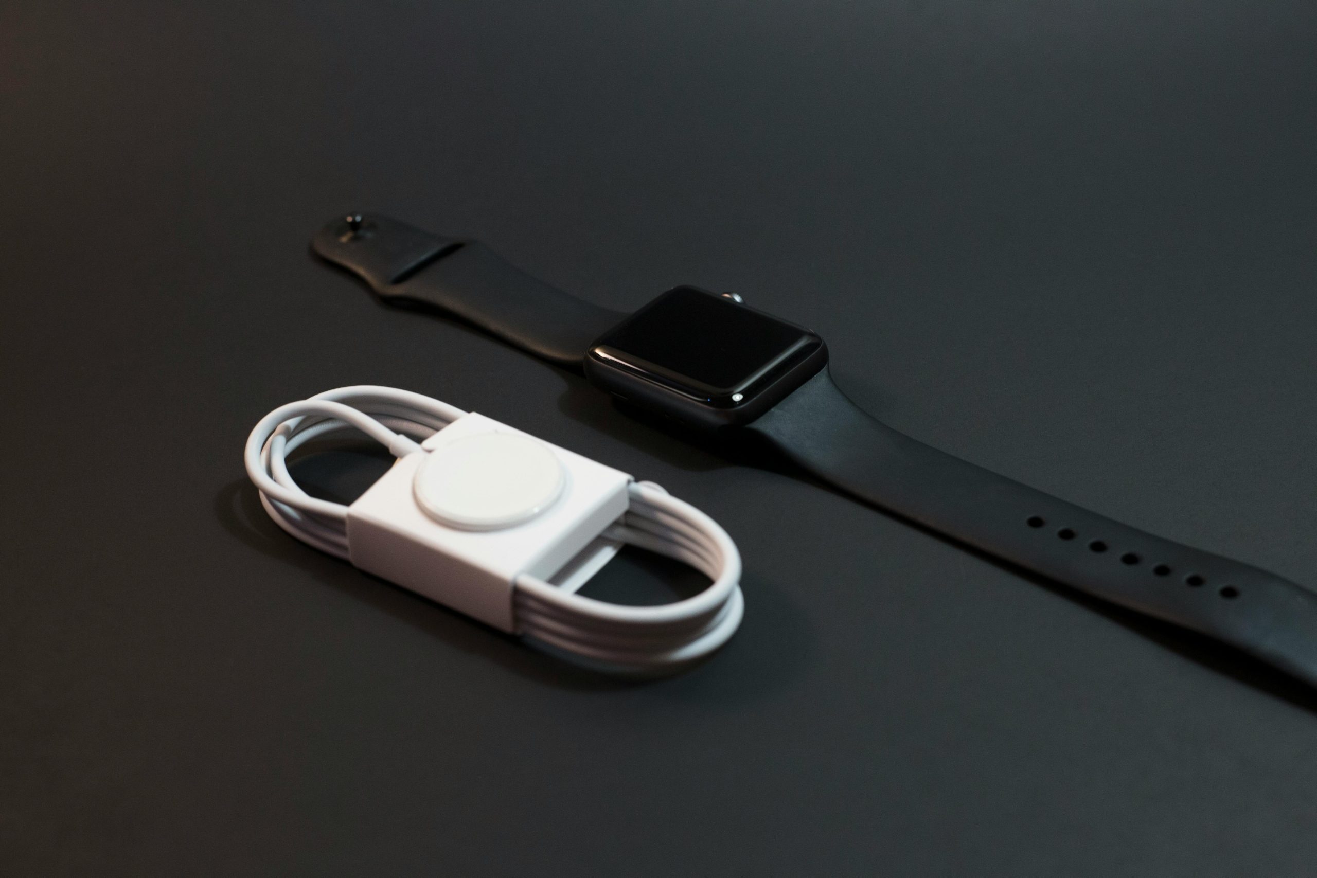 Close-up of a black smartwatch and white charging cable on a dark surface. Ideal for technology themes.